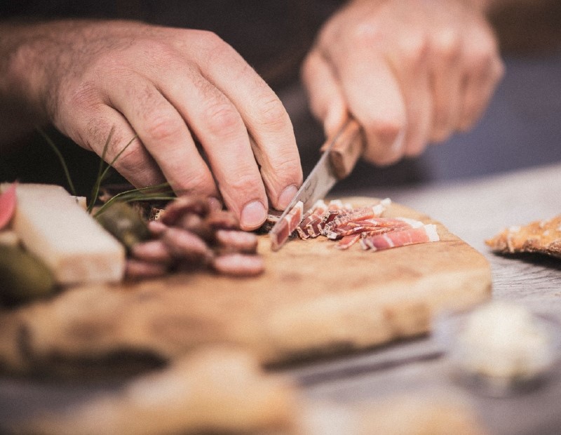 Mann schneidet den Speck in dünne Scheiben auf dem Schneidebrett.
