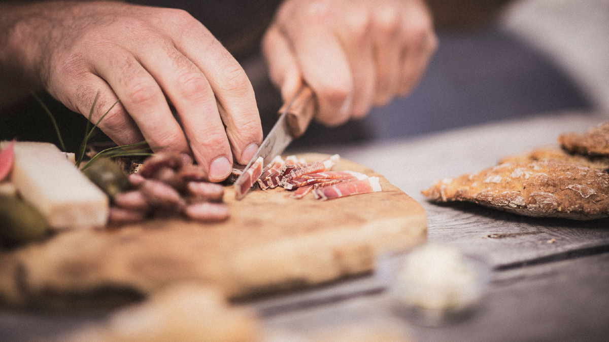 Mann schneidet den Speck in dünne Scheiben auf dem Schneidebrett.