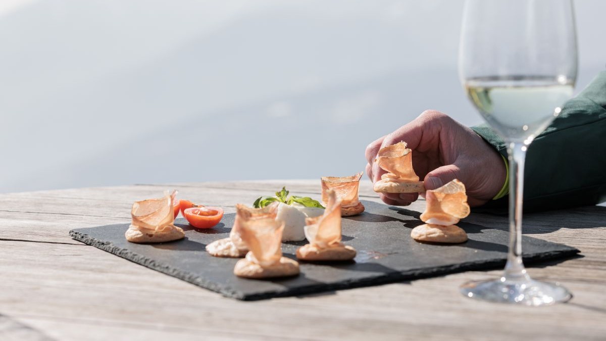 Un Apritivo di Speck con del vino bianco in su un tavolo di legno dietro le montagne innevate