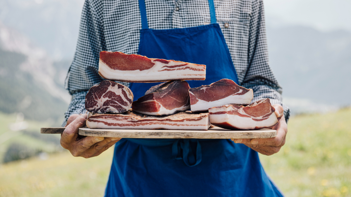 Un contadino tiene un tagliere con diverse varietà di Bauernspeck.