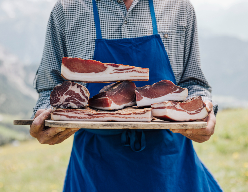 Ein Bauer hält ein Holzbrett mit verschiedenen Sorten Bauernspeck.