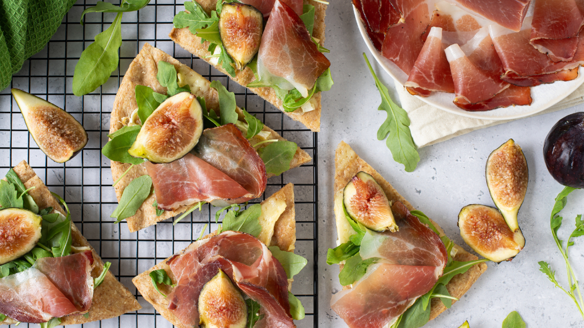 Focaccia integrale con Speck Alto Adige IGP, fichi freschi e rucola su una griglia da cucina.