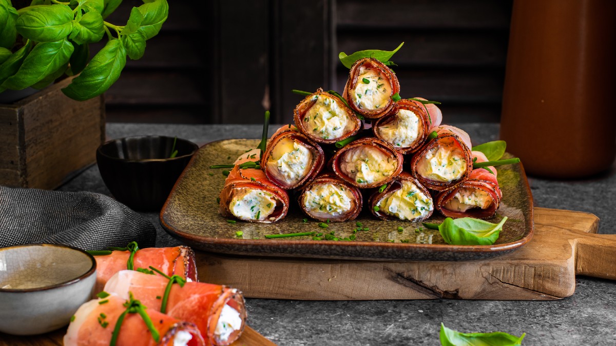 Involtini di Speck Alto Adige IGP con crema alle erbe, serviti su un piatto con erbe fresche.