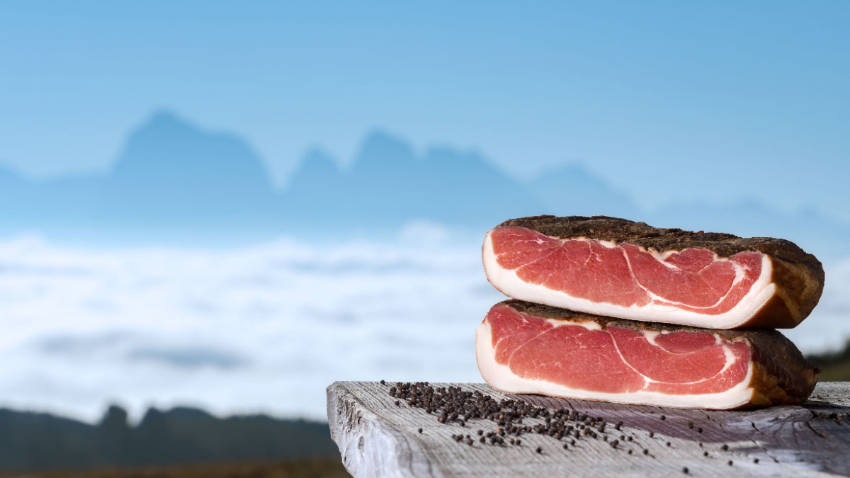 Due forme di speck una sopra l'altra con delle bacche di ginepro