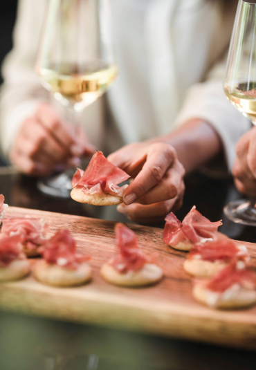 Aperitif mit Häppchen mit Speck und Gläsern Weißwein