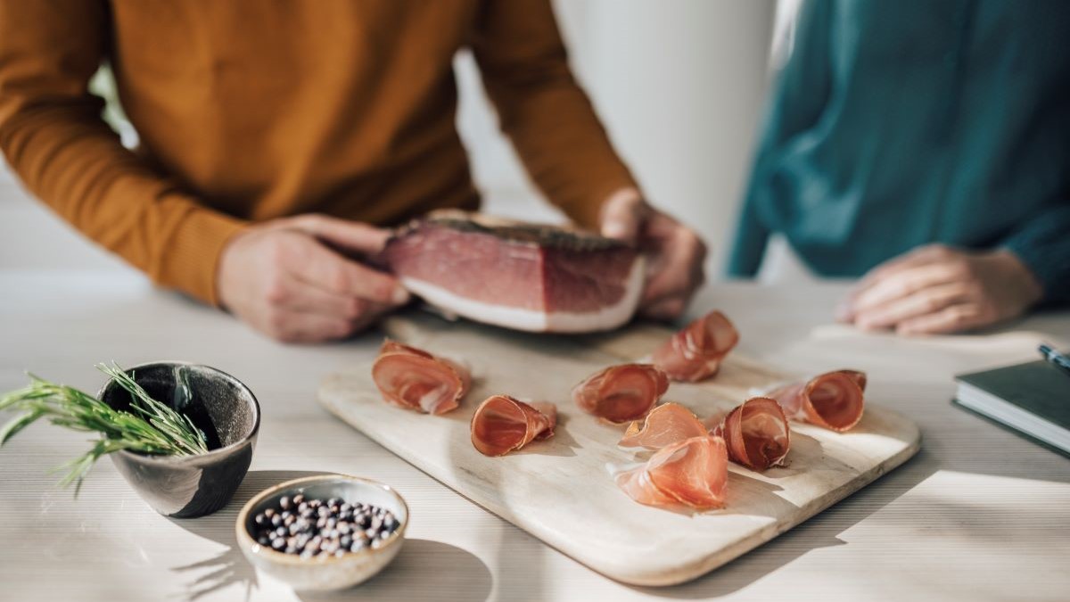 Pezzo di speck e fettine di speck sul tagliere