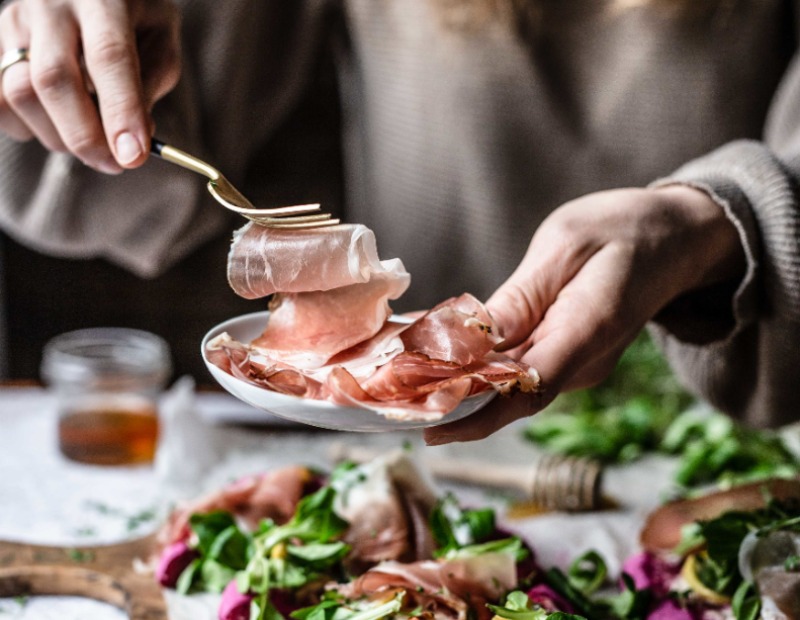 Dünne Scheiben Speck auf einem weißen Teller.