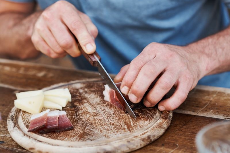 Uomo taglia pezzo di speck sul tagliere