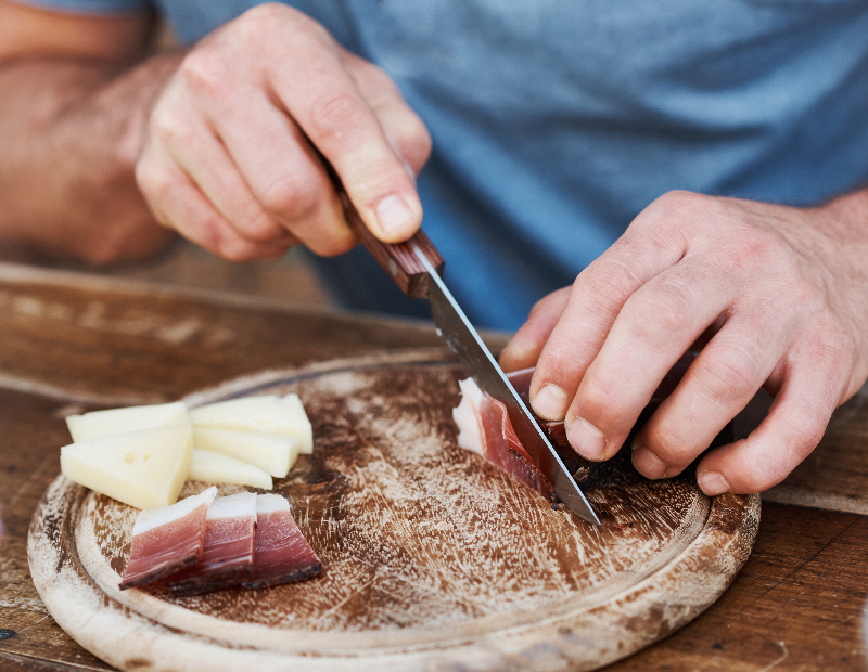 Eine Person schneidet Speck auf dem Schneidebrett.