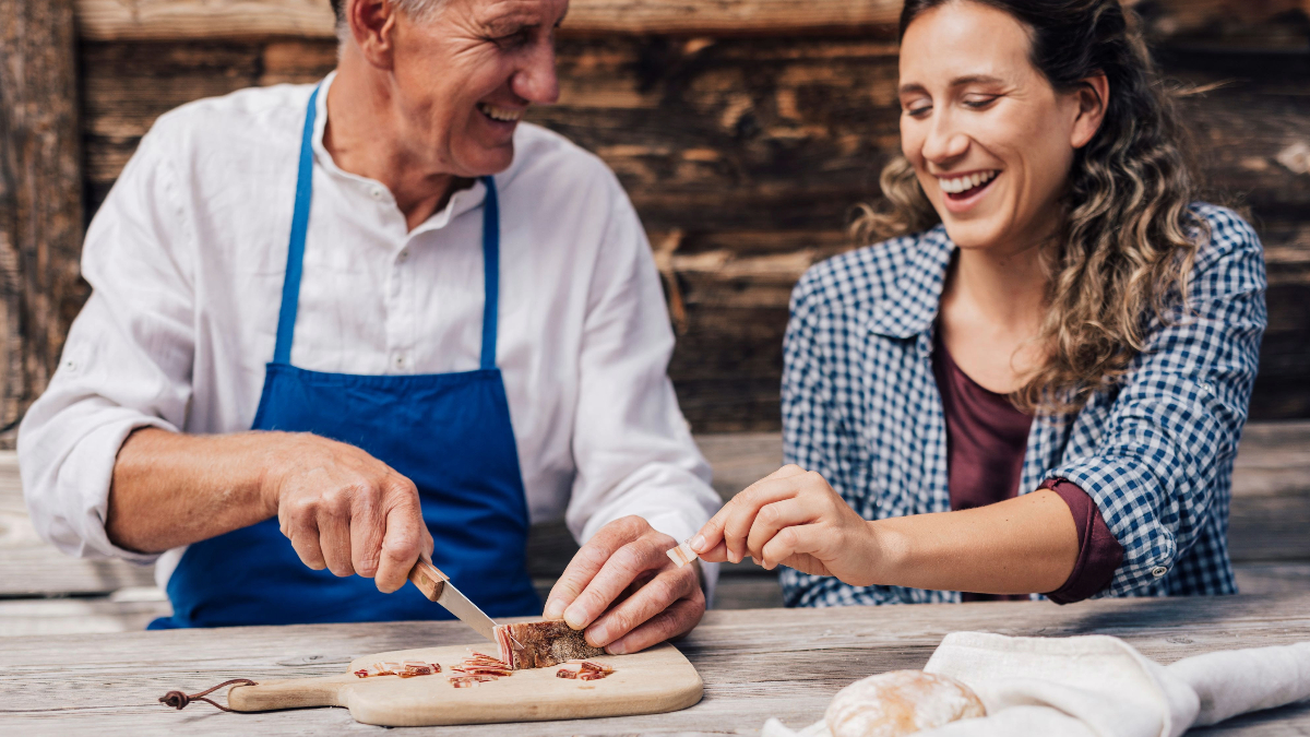 Un uomo ed una donna tagliano e mangiano lo speck insieme