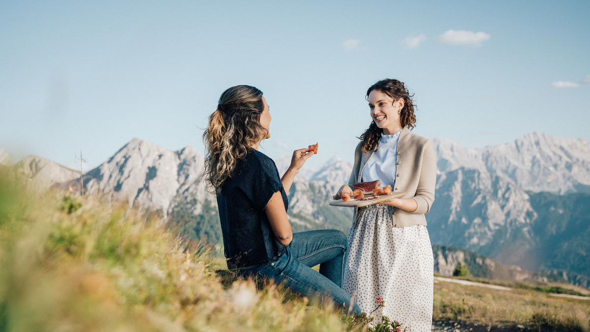 Zwei Mädchen essen Speck mit einem Berg im Hintergrund.