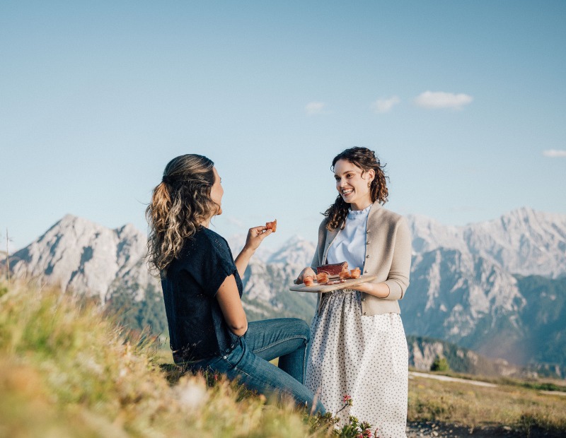 Zwei Mädchen essen Speck mit einem Berg im Hintergrund.