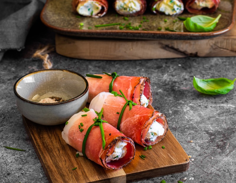 Un piatto pieno di involtini di Speck Alto Adige IGP con un ripieno di formaggio alle erbe.