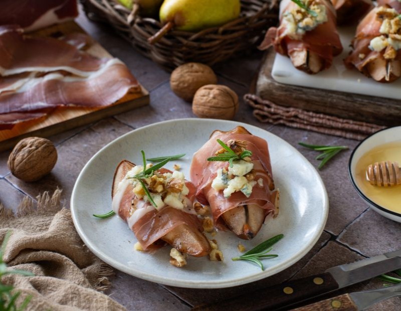 Roasted pears wrapped in Speck Alto Adige PGI with melted gorgonzola, honey and crunchy walnuts served on a plate